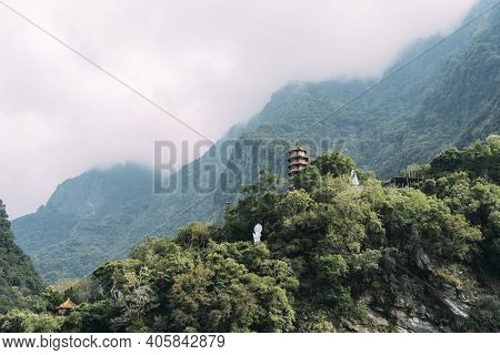 Landscape View Of Xiangde Temple From Valley Below With Sharp Cliffs Behind And Misty Sky.