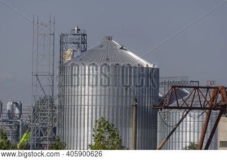 Construction Of A Modern Grain Terminal On A Blue Sky Background. Metal Cylindrical Silo And Support