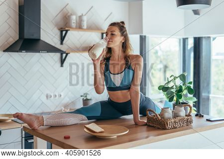Fit Woman Having Breakfast In Split Position On The Kitchen Table.