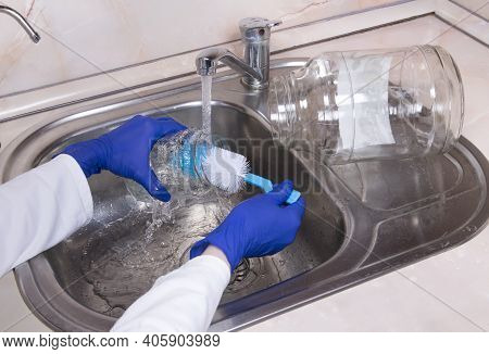 Woman's Hands With Gloves Washing Dish With Fresh Water At Kitchen Faucet Over The Metal Sink. Human