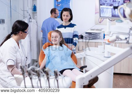 Dentist In Dental Office Telling Little Girl The Treatment Will Not Be Painfull. Child With Her Moth