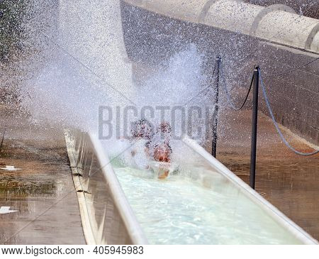 People Having Fun At Waterpark. There Are Legs Of Man Sliding Down Slide Under Water.