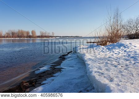 Section Of Wide Plain River Partially Covered With Thin Ice, Thick Ice Floes On The Shore On A Foreg