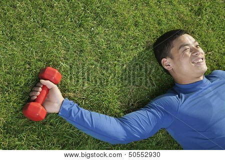 Young Athletic Man Lying Down in Grass with Dumbbells, Close Up