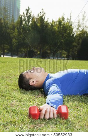 Young Athletic Man Lying Down in Park with Dumbbells, Vertical