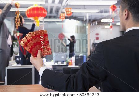 Businessman holding red envelopes and coworkers hanging decorations for Chinese new year