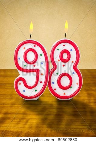 Burning birthday candle number 98 on a wooden background