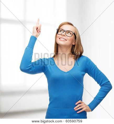 advertisement concept - attractive young woman in casual clothes and black eyeglasses pointing her finger up