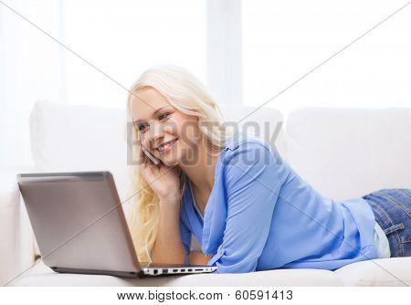 home, technology and internet concept - smiling woman with smartphone and laptop computer sitting on couch at home