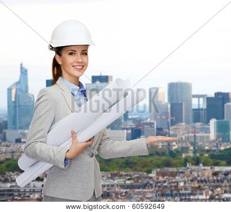 building, developing, consrtuction and architecture concept - smiling architect in helmet with blueprints showing something on palm of hand