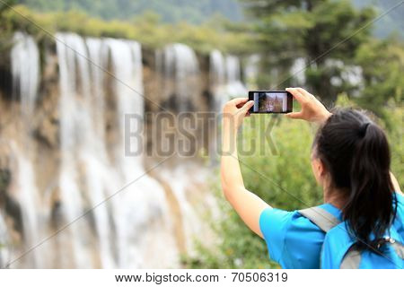 woman tourist taking photo with cellphone in jiuzhaigou national park,china