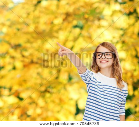 education, school and imaginary screen concept - cute little girl in eyeglasses pointing in the air or imaginary screen