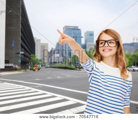education, school and imaginary screen concept - cute little girl in eyeglasses pointing in the air or imaginary screen