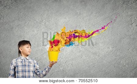 Young boy splashing colorful paint from bucket