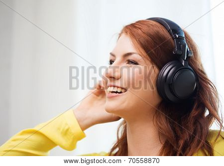 technology, music and happiness concept - smiling teenage girl in headphones at home