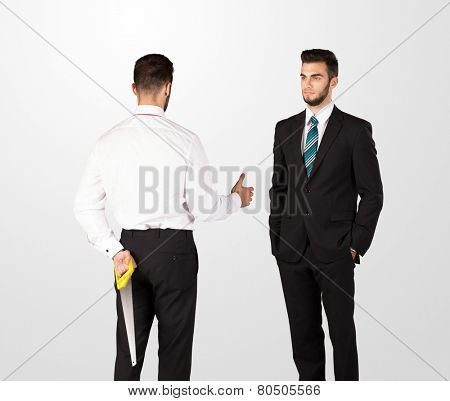 Two opposing businessman shake hands, one of them hiding a weapon behind his back