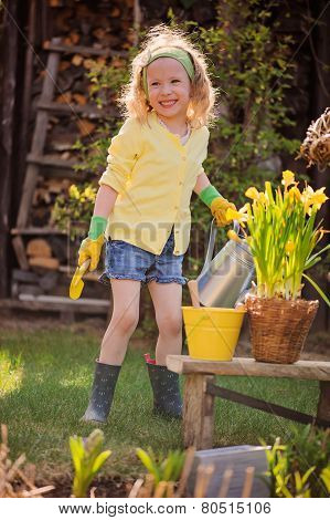 adorable happy child girl playing little gardener and holding watering can in spring garden