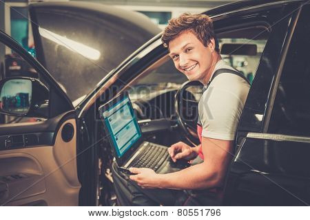 Serviceman making car diagnostics with laptop in a workshop