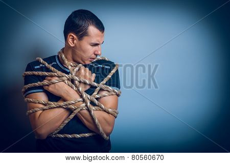 the man of European appearance brunet tied with rope on a gray b