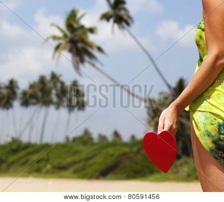 Woman holding red heart on exotic sandy beach - Love concept