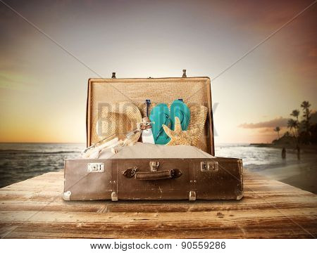Travel concept with old suitcase on wooden planks full of beach accessories. Placed on mole with sandy beach on background