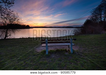 Colorful Sunset Over Lake Shore With Bench