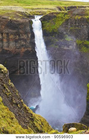 Spectacular waterfall Hayfoss in Iceland. Vertical cliff, from which the powerful waterfall flies on black stones