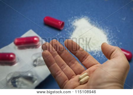 Right hand with pills and capsules, in the blue background  red capsules tablet