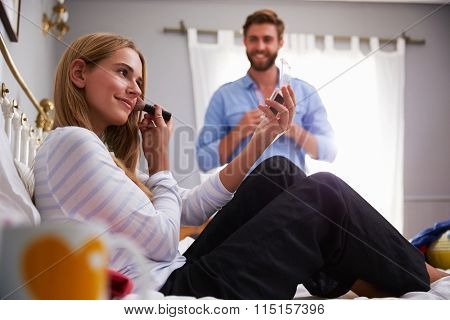 Woman Puts On Make Up As Man Gets Dressed In Bedroom