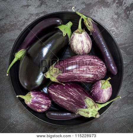 Eggplant varieties in black bowl over dark slate background.  Overhead view.