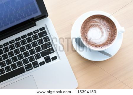A Cup Of Coffee In A White Cup And Computer Labtop On Mable Table