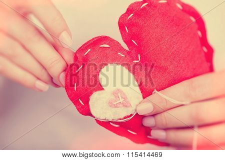Woman sews red heart shaped toy by needle, body part, conceptual symbol of love and soul pain treatment, happy Valentine day