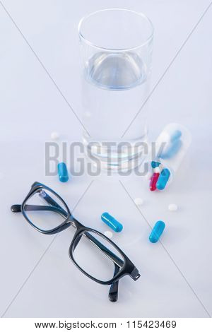 Water glass, pills and eyeglasses on the surface.