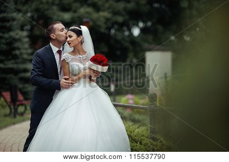 Newlywed Valentynes Posing And Hugging In A Romantic European Park With Roses Bouquet