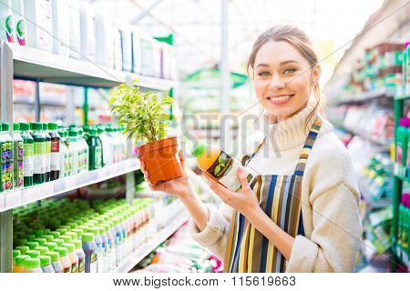 Happy charming young woman gardener buying agricultural chemicals for plants in shop
