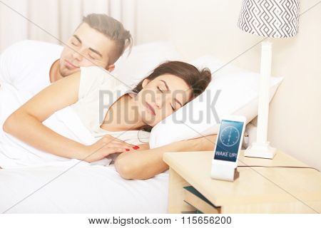 Young couple waking up with mobile alarm clock