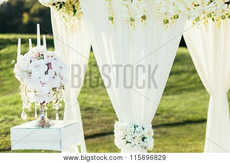 wedding arch with flowers and ?andle decoration on sunny day in ceremony place