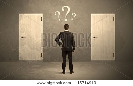 Salesman standing in front of two doors, unable to make the right decision concept with question marks above his head