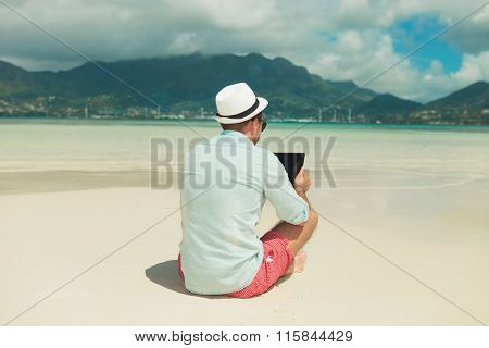 man sitting in the sand with legs crossed while reading from ipad in an exotic place