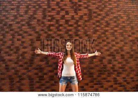 Young Girl Standing With Opened Hands On The Bakground Of Brik Wall