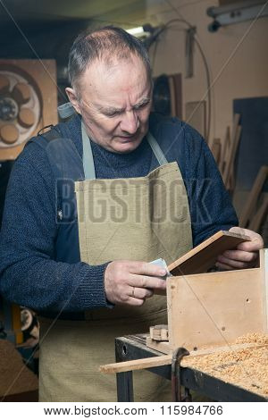 Men sandpaper grinds wood product in a workshop