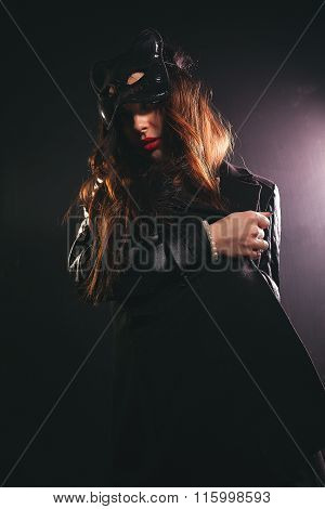A young girl in the studio in a black coat and a mask sexy cat