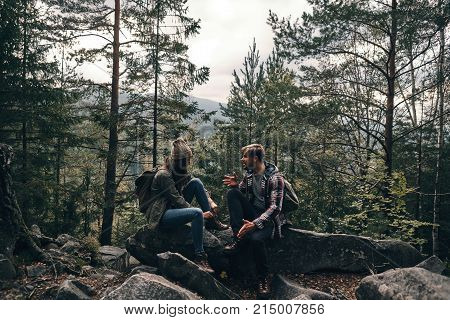 Finally enjoying the travel. Beautiful young couple sitting on the rocks and talking while hiking together in the woods