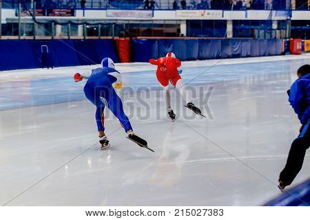 back two men speed skaters race and coach on ice rink