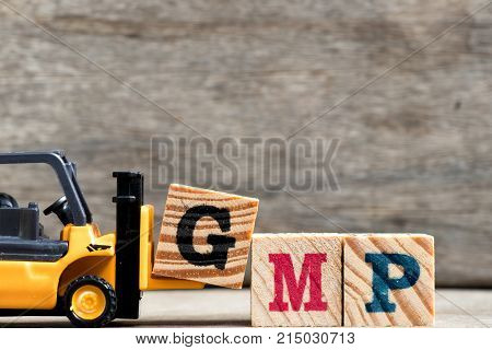 Yellow plastic forklift hold letter G to complete word GMP (Abbreviation of Good Manufacturinc Practice) on wood background