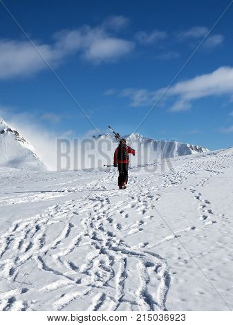 Skier with skis on his shoulder go up to top of snowy mountain in nice sun day. Caucasus Mountains in winter Georgia region Gudauri Mt. Kudebi.