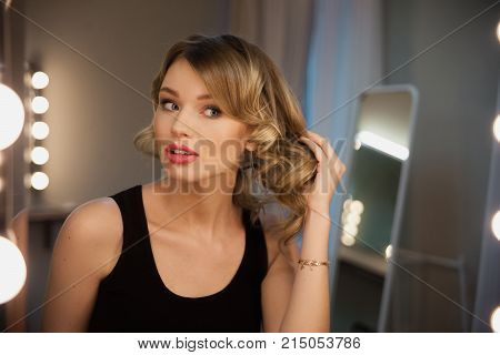 Attractive Blonde Girl Primp At The Mirror With Lamps In The Beauty Studio.