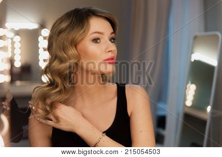 Attractive Blonde Girl Primp At The Mirror With Lamps In The Beauty Studio.