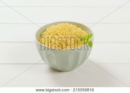 bowl of uncooked alphabet pasta on white wooden background