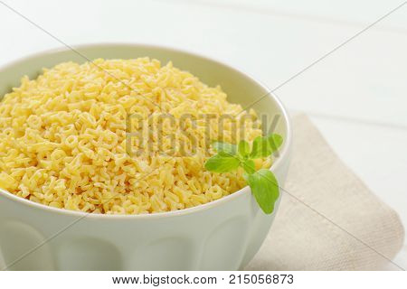 bowl of uncooked alphabet pasta on beige place mat - close up